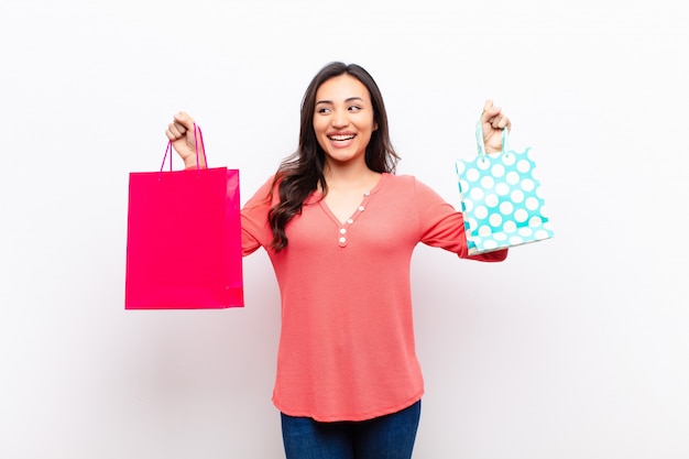 Young latin pretty woman  against flat wall with shopping bags