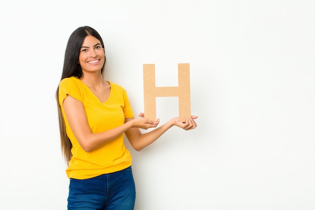 Young latin pretty woman excited, happy, joyful, holding the letter H of the alphabet to form a word or a sentence.