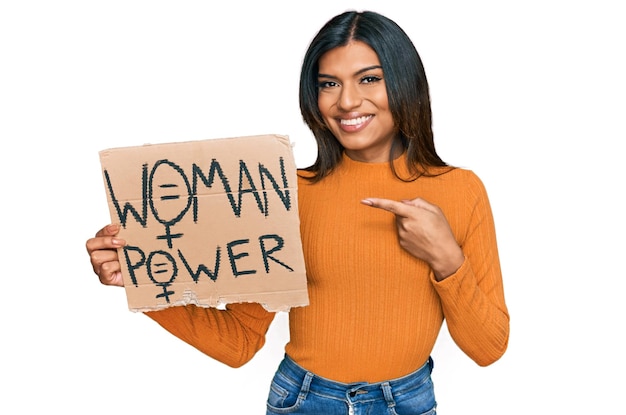 Young latin transsexual transgender woman holding woman power banner smiling happy pointing with hand and finger