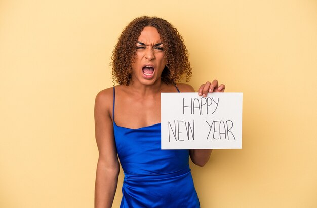 Молодая латинская транссексуальная женщина празднует Новый год на желтом фоне кричит очень сердито и агрессивно.