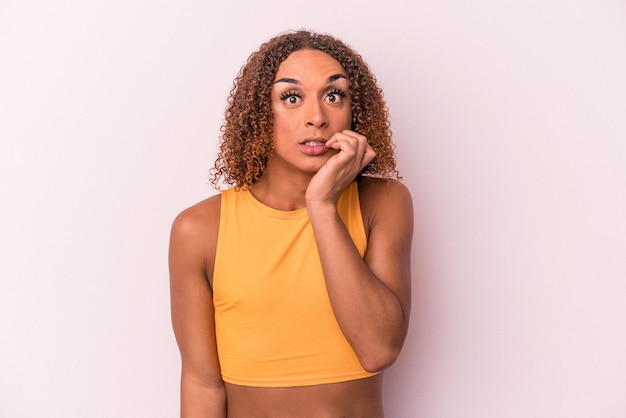 Young latin transsexual woman isolated on pink background biting fingernails, nervous and very anxious.