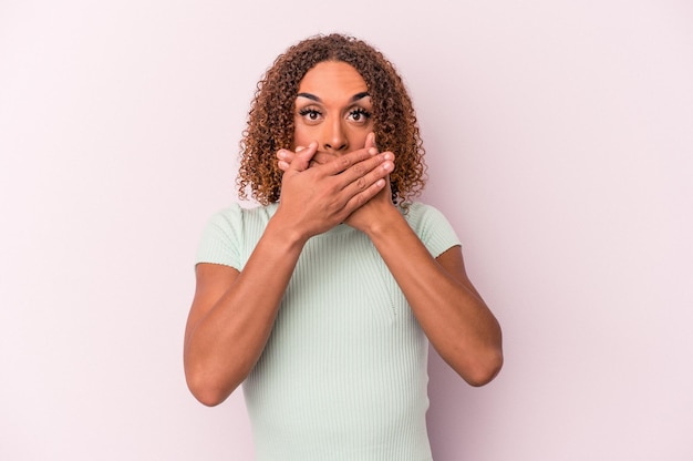 Young latin transsexual woman isolated on pink background covering mouth with hands looking worried.