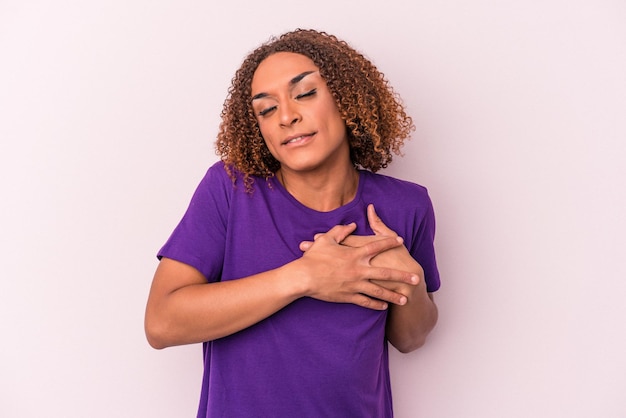 Young latin transsexual woman isolated on pink background has friendly expression, pressing palm to chest. Love concept.