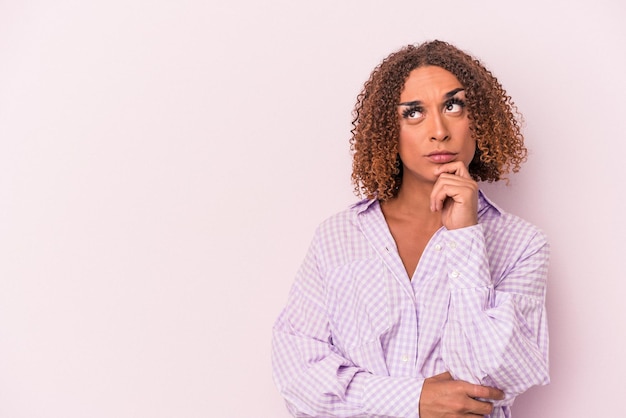 Young latin transsexual woman isolated on pink background looking sideways with doubtful and skeptical expression.