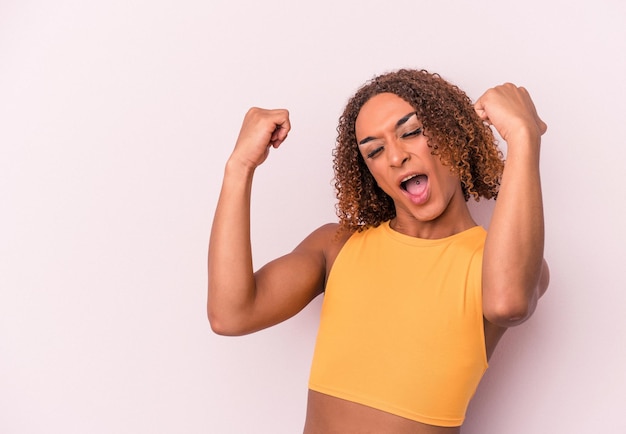 Young latin transsexual woman isolated on pink background raising fist after a victory, winner concept.