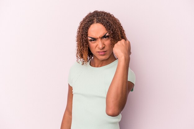 Young latin transsexual woman isolated on pink background showing fist to camera, aggressive facial expression.