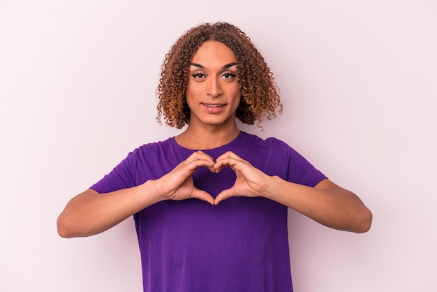 Young latin transsexual woman isolated on pink background smiling and showing a heart shape with hands.