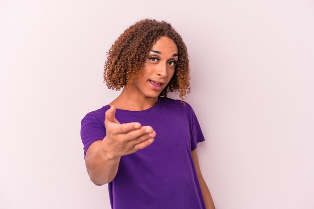 Young latin transsexual woman isolated on pink background stretching hand at camera in greeting gesture.