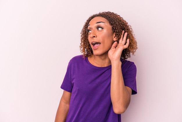 Young latin transsexual woman isolated on pink background trying to listening a gossip.