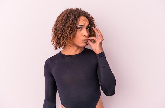 Young latin transsexual woman isolated on pink background with fingers on lips keeping a secret.