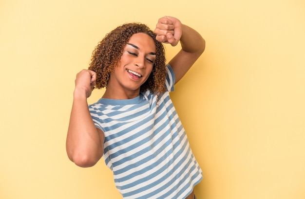 Young latin transsexual woman isolated on yellow background celebrating a special day, jumps and raise arms with energy.