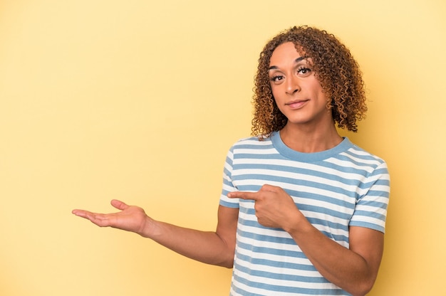 Photo young latin transsexual woman isolated on yellow background excited holding a copy space on palm.