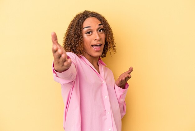 Young latin transsexual woman isolated on yellow background feels confident giving a hug to the camera.