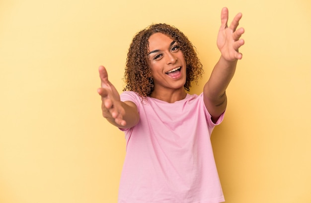 Young latin transsexual woman isolated on yellow background feels confident giving a hug to the camera