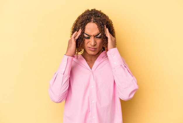 Young latin transsexual woman isolated on yellow background having a head ache, touching front of the face.