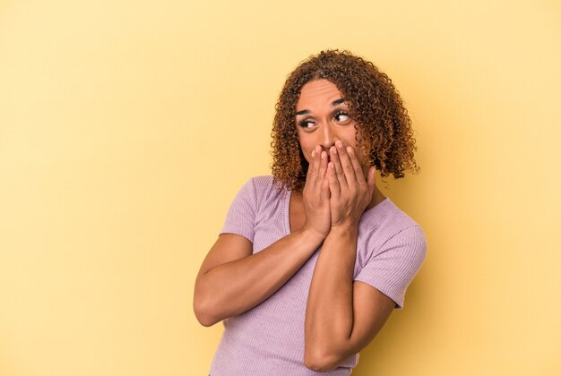 Young latin transsexual woman isolated on yellow background laughing about something, covering mouth with hands.