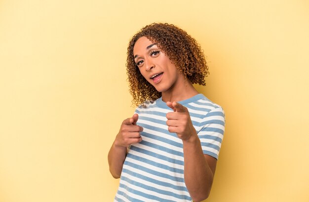 Young latin transsexual woman isolated on yellow background pointing to front with fingers.