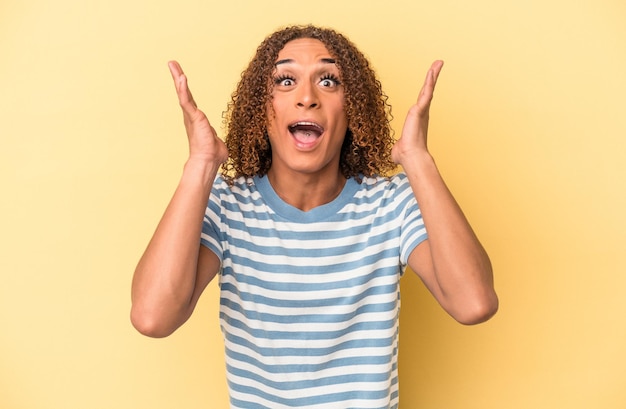 Young latin transsexual woman isolated on yellow background receiving a pleasant surprise, excited and raising hands.