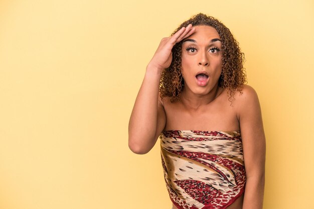 Young latin transsexual woman isolated on yellow background\
shouts loud, keeps eyes opened and hands tense.