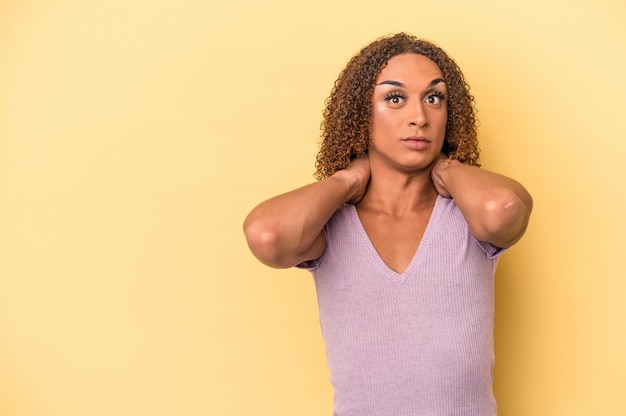 Young latin transsexual woman isolated on yellow background touching back of head, thinking and making a choice.