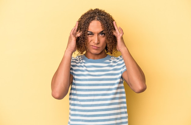 Young latin transsexual woman isolated on yellow background touching temples and having headache.