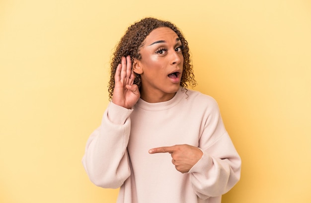 Young latin transsexual woman isolated on yellow background trying to listening a gossip.