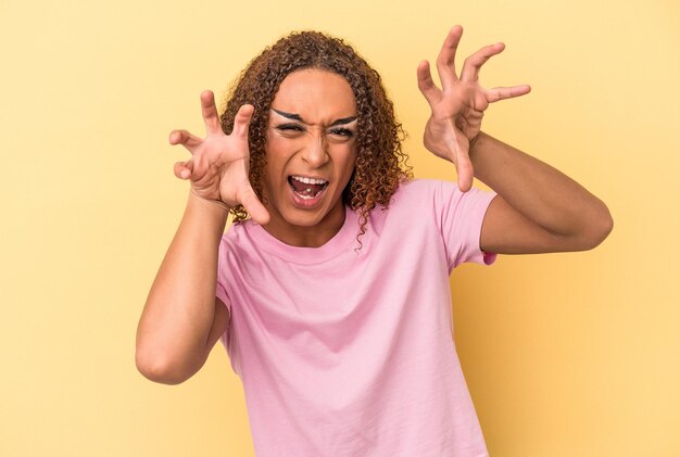 Young latin transsexual woman isolated on yellow background upset screaming with tense hands.