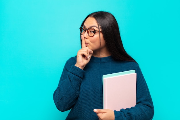 Young latin woman asking for silence and quiet, gesturing with finger in front of mouth, saying shh or keeping a secret