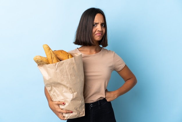 Young latin woman buying some breads isolated on blue angry