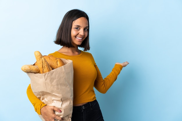 Молодая латинская женщина покупает хлеб, изолированные на синем фоне