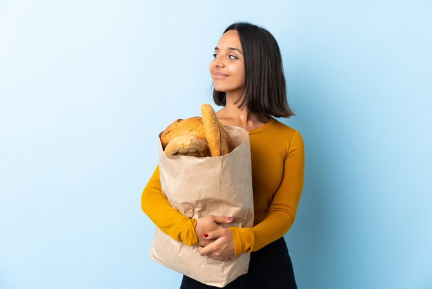 Young latin woman buying some breads isolated on blue looking side