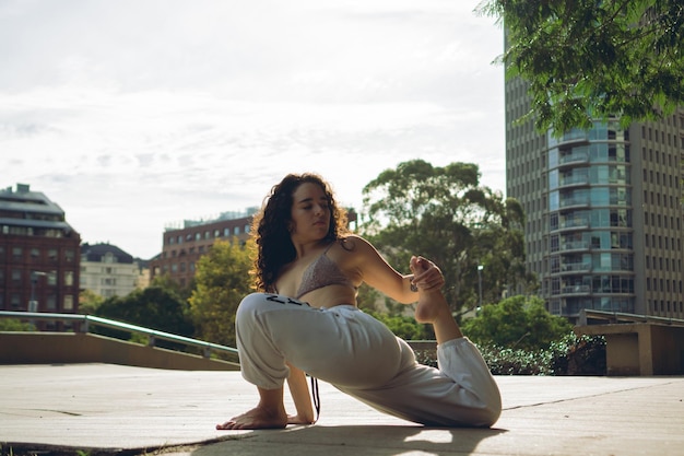 Young latin woman in a city park stretching doing hip opening Eka Pada Rajakapotasana exercise or One Legged King Pigeon pose