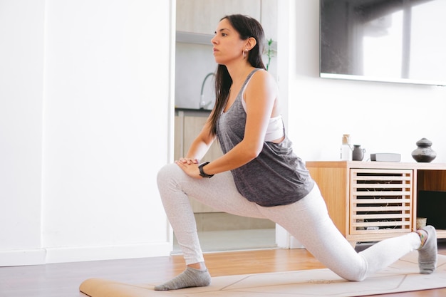 Young latin woman doing Bulgarian squat in her living room Copy space