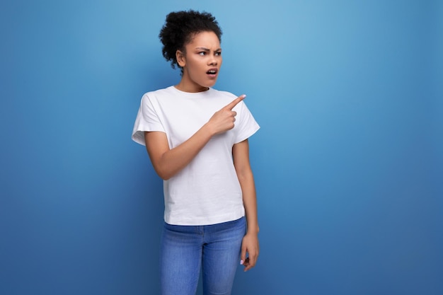 Young latin woman dressed in a white tank top with a mockup points her hand to the side