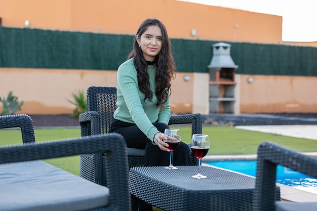 Foto giovane donna latina che beve vino nel giardino della villa al tramonto