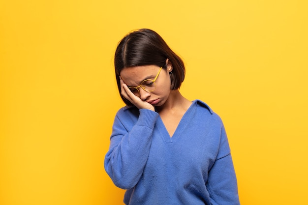 Young latin woman feeling bored, frustrated and sleepy after a tiresome, dull and tedious task, holding face with hand