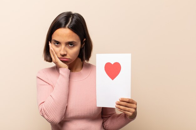 Young latin woman feeling bored, frustrated and sleepy after a tiresome, dull and tedious task, holding face with hand