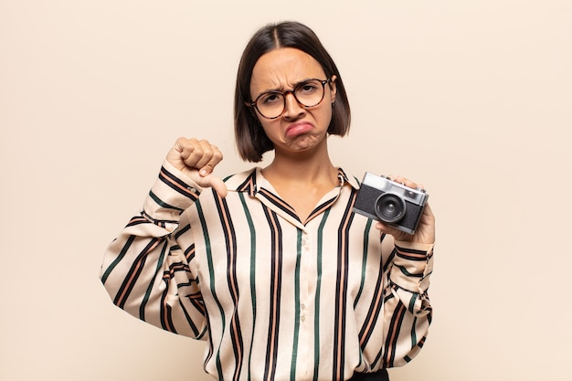 Foto giovane donna latina che si sente arrabbiata, arrabbiata, infastidita, delusa o scontenta, mostrando il pollice verso il basso con uno sguardo serio