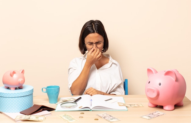 Young latin woman feeling disgusted, holding nose to avoid smelling a foul and unpleasant stench