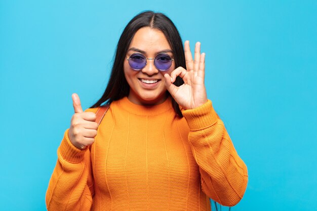 Young latin woman feeling happy, amazed, satisfied and surprised, showing okay and thumbs up gestures, smiling