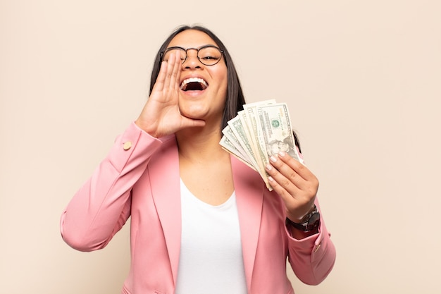 Young latin woman feeling happy, excited and positive, giving a big shout out with hands next to mouth, calling out