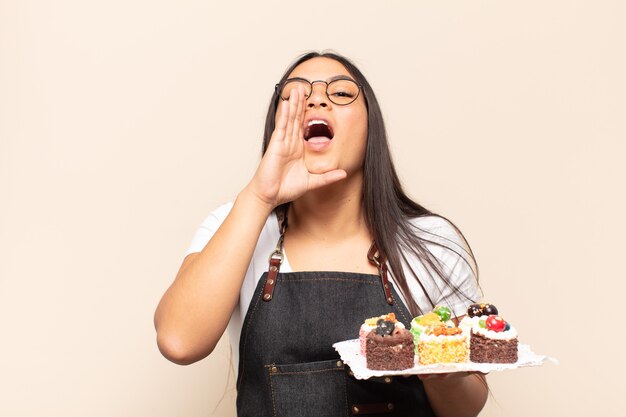 Young latin woman feeling happy, excited and positive, giving a big shout out with hands next to mouth, calling out