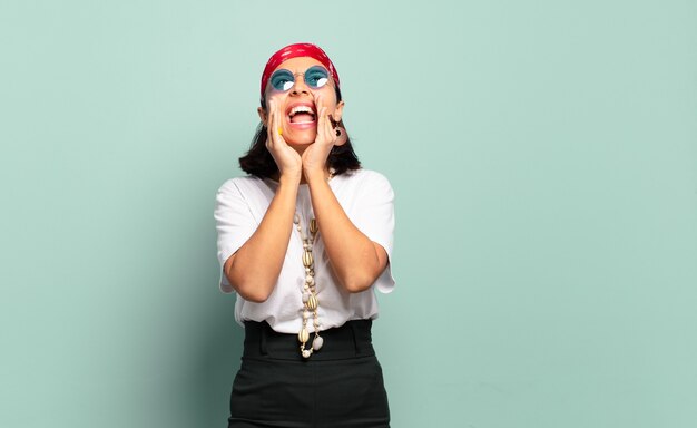 Young latin woman feeling happy, excited and positive, giving a big shout out with hands next to mouth, calling out