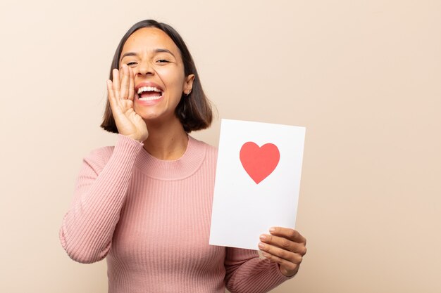 Young latin woman feeling happy, excited and positive, giving a big shout out with hands next to mouth