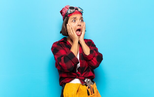 Young latin woman feeling happy, excited and surprised, looking to the side with both hands on face