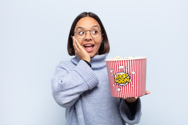 Young latin woman feeling happy, excited and surprised, looking to the side with both hands on face