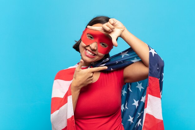 Photo young latin woman feeling happy, friendly and positive, smiling and making a portrait or photo frame with hands