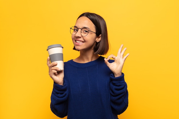 Young latin woman feeling happy, relaxed and satisfied, showing approval with okay gesture, smiling