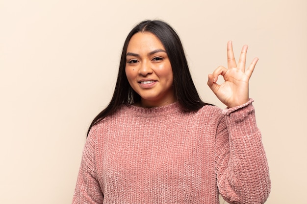 Young latin woman feeling happy, relaxed and satisfied, showing approval with okay gesture, smiling