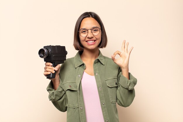 Young latin woman feeling happy, relaxed and satisfied, showing approval with okay gesture, smiling